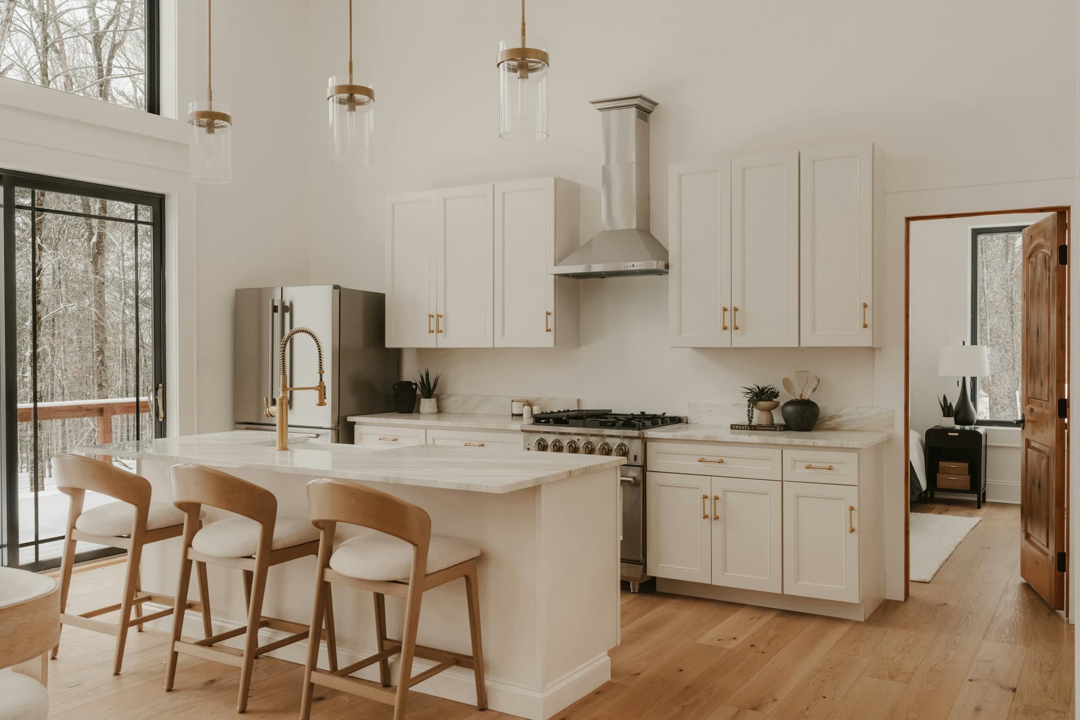 Light-filled kitchen with pale cabinetry, a stone island and warm timber stools.