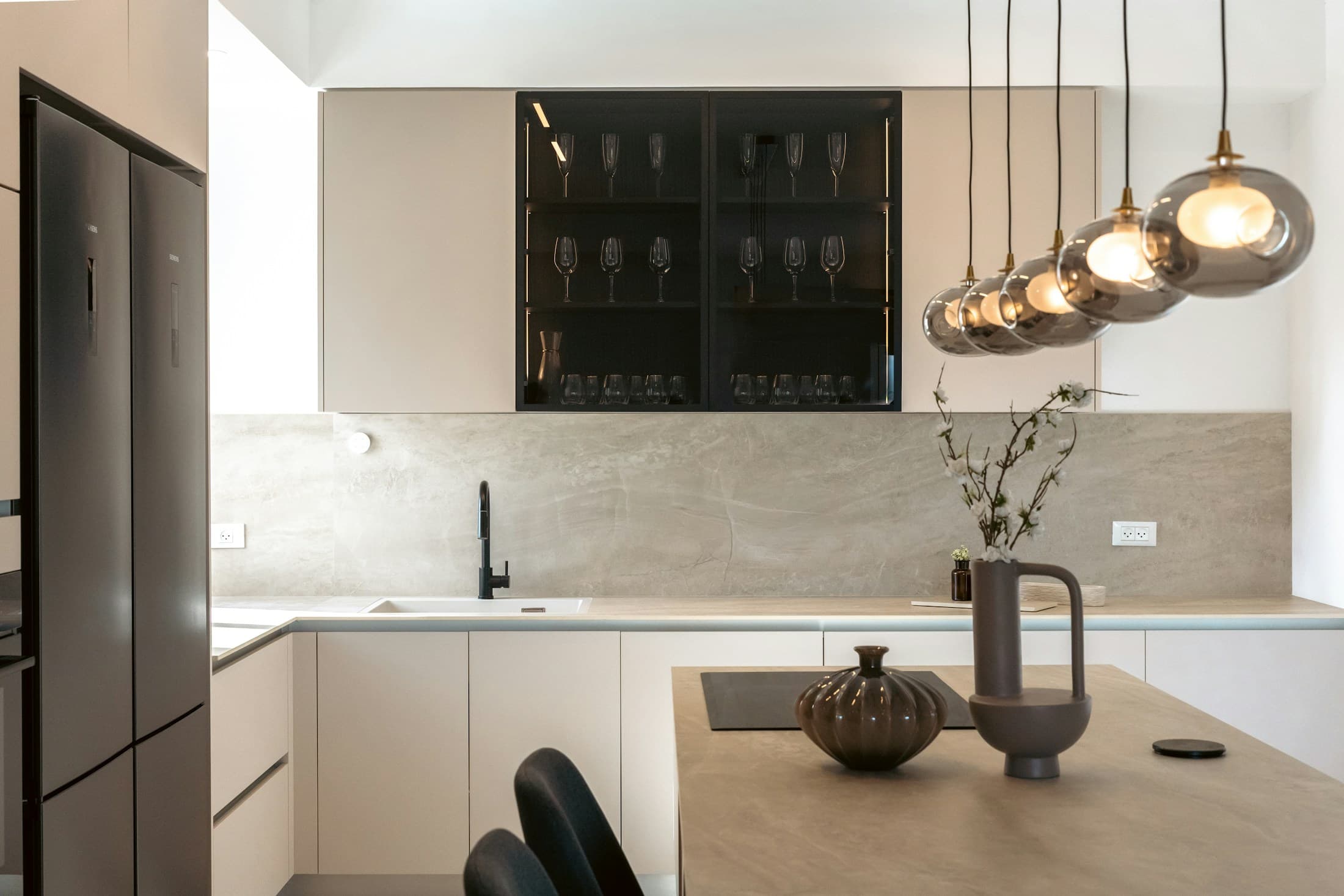 Moody modern kitchen with stone surfaces, glass-front cabinetry and pendant lighting